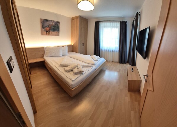 A hotel room with a bed, a bedside table, a TV, and a painting on the wall.