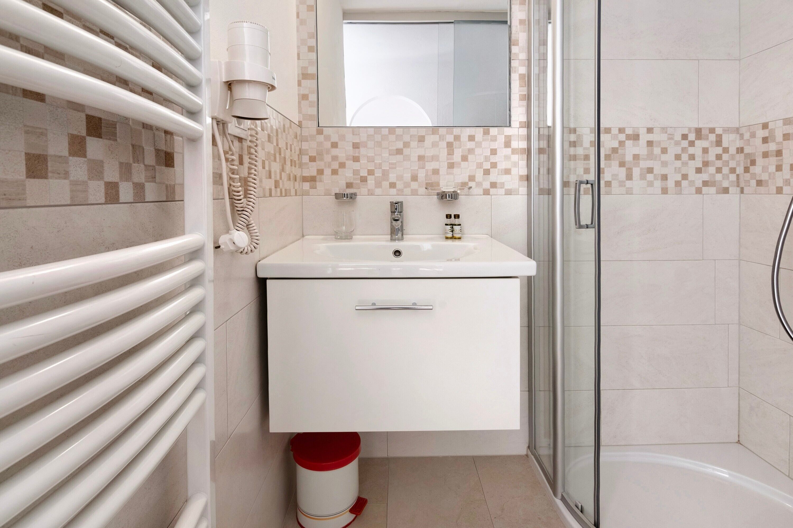 Une salle de bain avec un lavabo blanc, un miroir, une douche en verre et un sol carrelé.