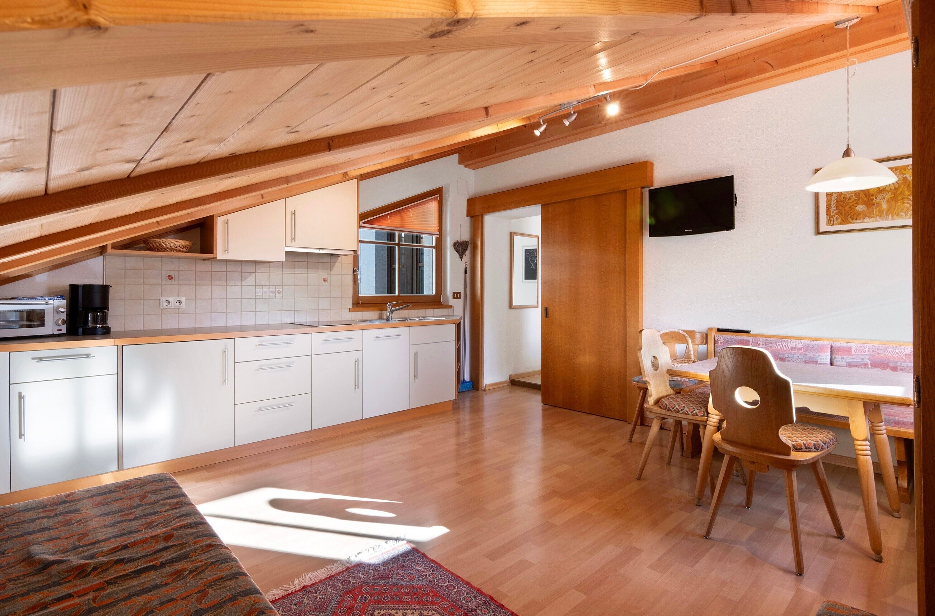 Une cuisine avec des armoires blanches, un plafond en bois et un coin repas comprenant des chaises et une table en bois.