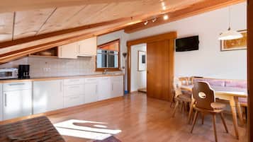 Une cuisine avec des armoires blanches, un plafond en bois et un coin repas comprenant des chaises et une table en bois.