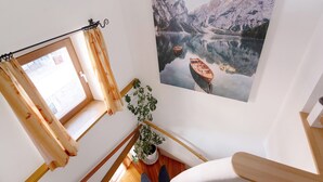 Una escalera con barandilla de madera, una planta en maceta y un ventanal con cortinas.