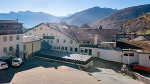 Un edificio con techo plano, zona de estacionamiento y montañas al fondo.