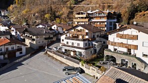 Un conjunto de edificios tradicionales de estilo europeo, con balcones, un área pavimentada central y montañas al fondo.