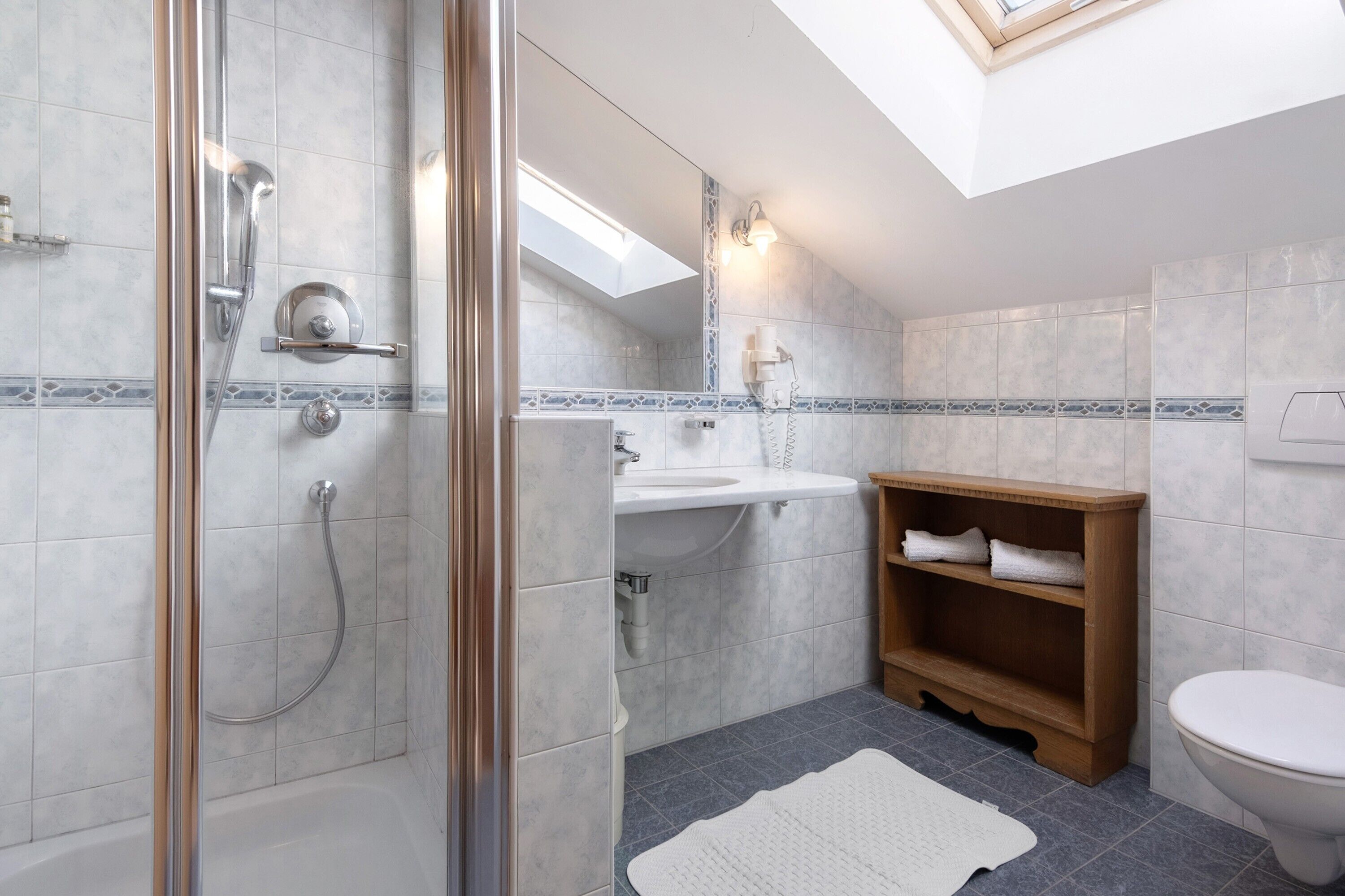 A modern bathroom with a glass shower enclosure, a white sink, and a wooden vanity.