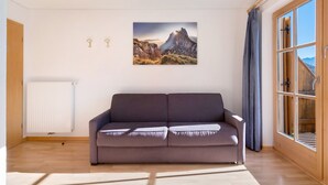 Una sala de estar moderna con un sofá, un ventanal grande y una pintura de un paisaje montañoso.