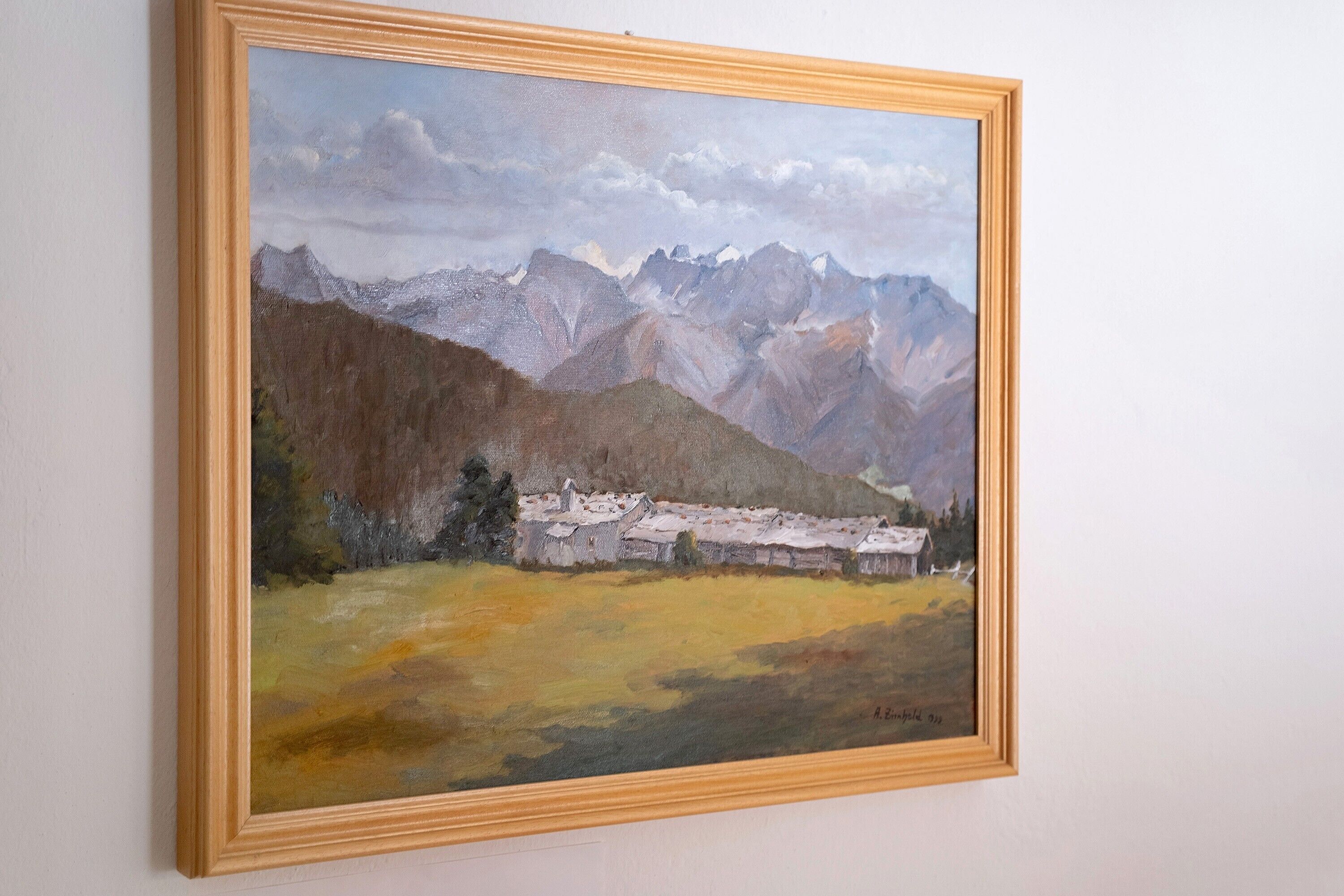 Un tableau représentant un paysage, encadré, avec des montagnes et un bâtiment.
