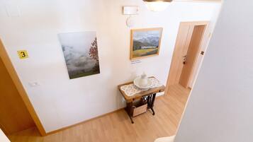 A hallway with a wooden floor, a table with a white vase, and two framed pictures on the wall.