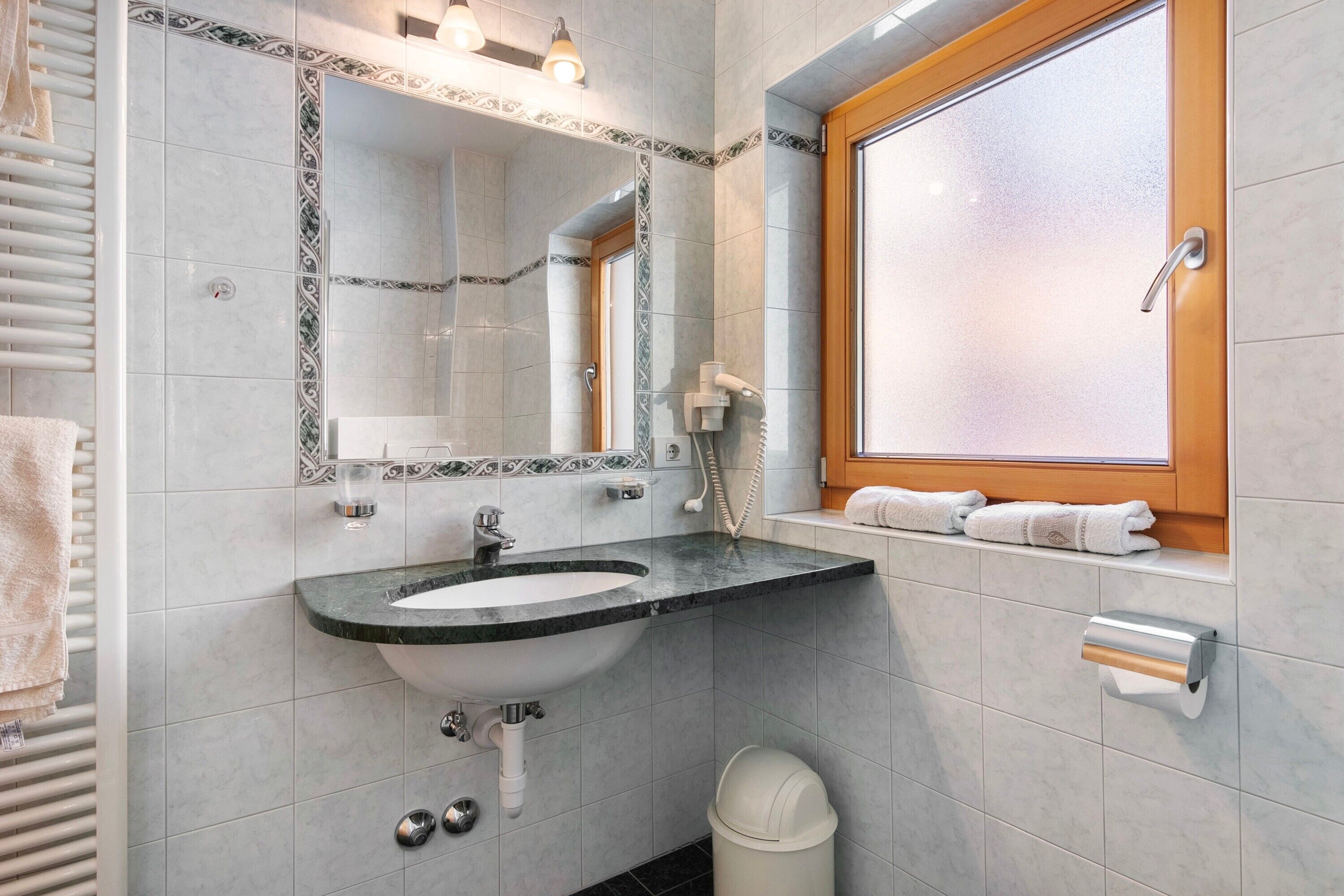 Une salle de bain équipée d’un lavabo, d’un miroir, d’un porte-serviettes et d’une fenêtre.