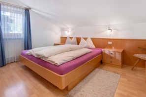 A bedroom with a bed, wooden headboard, bedside tables, a chair, and a window with curtains. - Apartment 'Haus Peer D1' with Mountain View, Balcony and Wi-Fi (Mals)