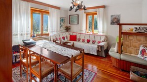 A cozy living room with a wooden dining table, chairs, a sofa with heart-patterned cushions, and a wooden cabinet. - Apartment 'Mulaz' with Mountain View, Shared Garden and Wi-Fi (Falcade)