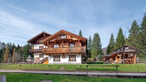 A large wooden chalet with multiple balconies, a stone foundation, and a surrounding forest. - Apartment 'Mulaz' with Mountain View, Shared Garden and Wi-Fi (Falcade)