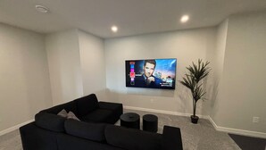 Un salon moderne avec un canapé d’angle noir, un téléviseur à écran plat fixé au mur et une plante en pot.