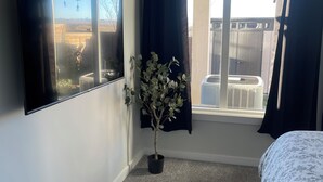 Une chambre à coucher avec un lit, une plante en pot, une fenêtre avec des rideaux et un téléviseur fixé au mur.
