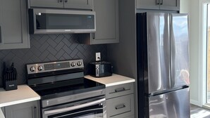Une cuisine moderne avec des armoires grises, des appareils en acier inoxydable et un dosseret orné d’un motif en chevrons.