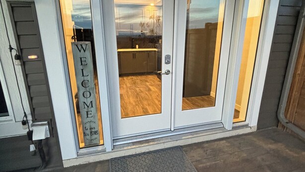 Une entrée avec une pancarte « BIENVENUE », un espace cuisine visible et une porte dotée d’un panneau en verre.