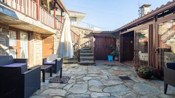 A stone-floored courtyard with wicker furniture, a wooden staircase, and a view of the surrounding buildings.