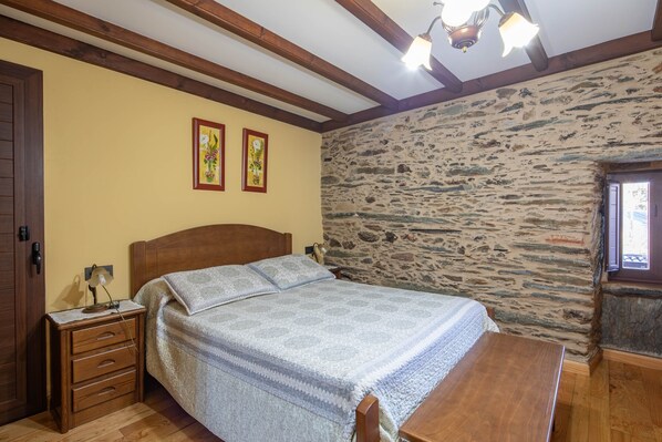 A bedroom with a wooden bed, a nightstand, a stone wall, and a window.