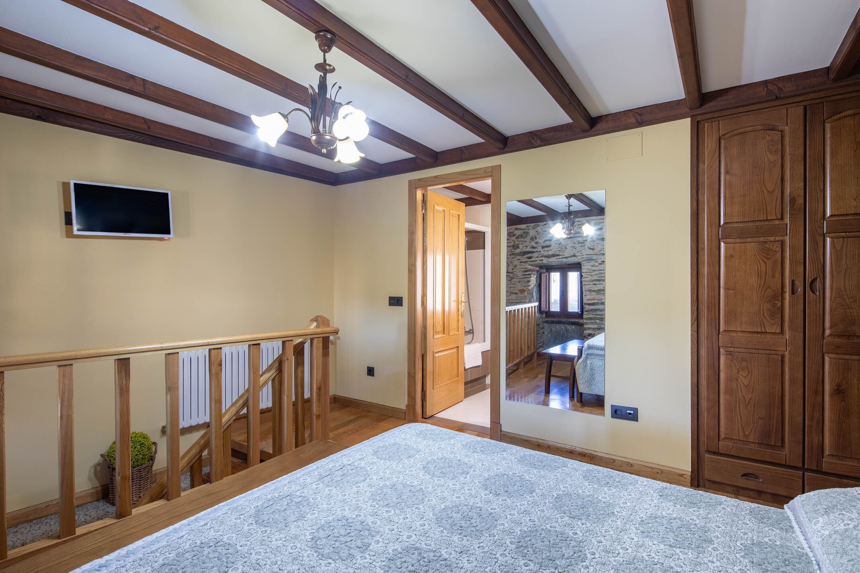 A room with a wooden staircase, a large bed, a wardrobe, and a television on the wall.