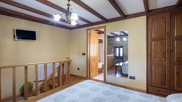 A room with a wooden staircase, a large bed, a wardrobe, and a television on the wall.