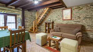 A rustic interior with a wooden staircase, a sofa, a dining table with chairs, and a stone wall.