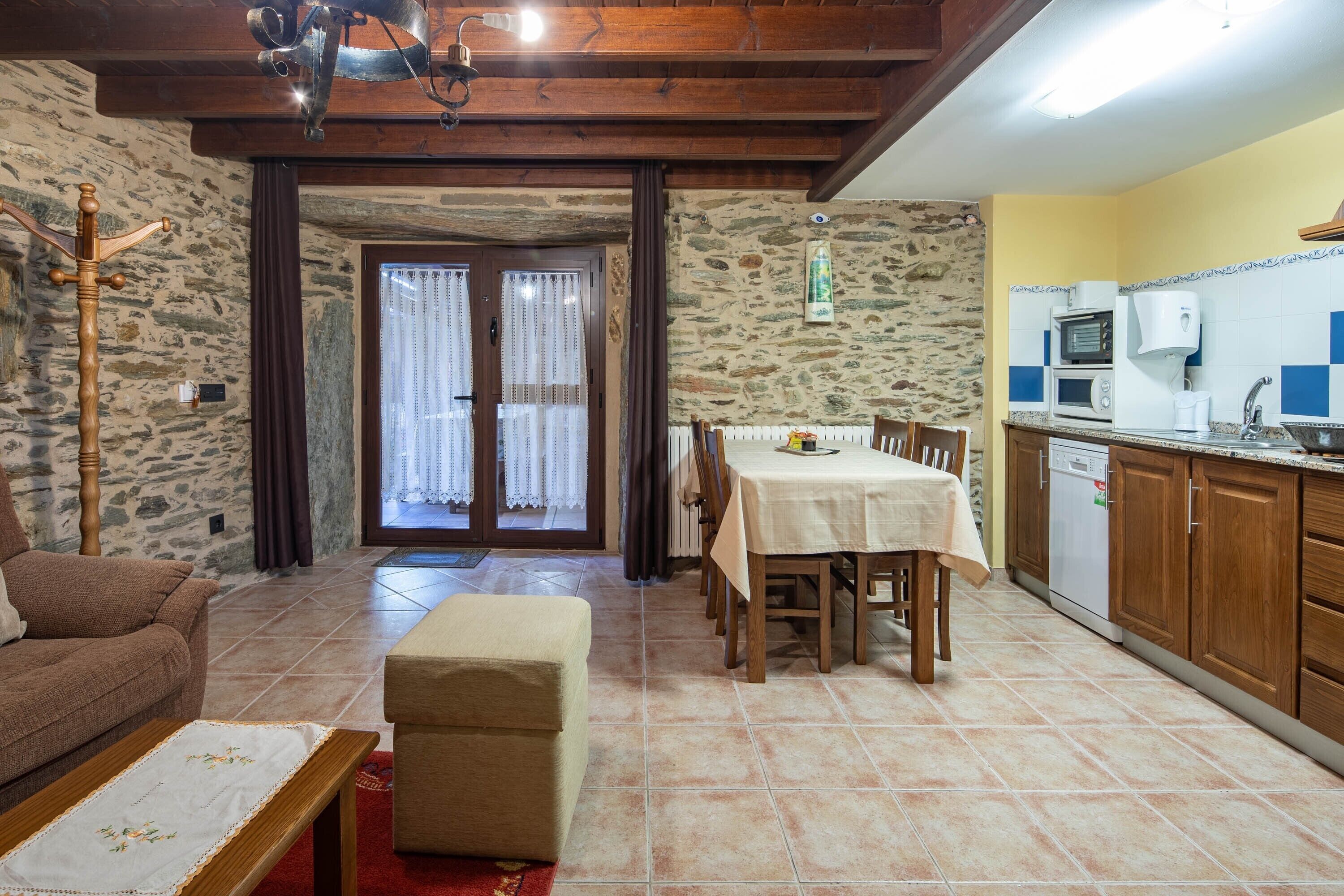 A living room with a sofa, a table, and a bench. There is a kitchen area with a sink, a stove, and a microwave.