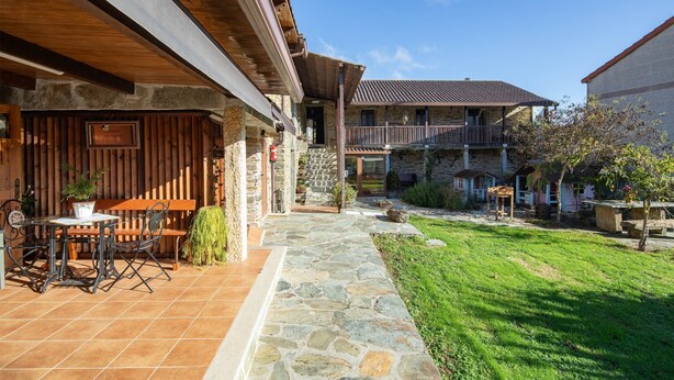 Un patio in pietra con posti a sedere all'aperto, un pergolato in legno e un vialetto in pietra che conduce a un edificio con tetto in tegole.