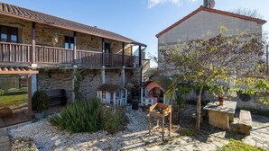 Un edificio in pietra con un balcone, un piccolo giardino con piante e una panchina, e un albero.