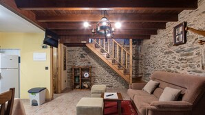 Un interno rustico con una scala in legno, un muro in pietra, un divano, un tavolino e un televisore montato a parete.