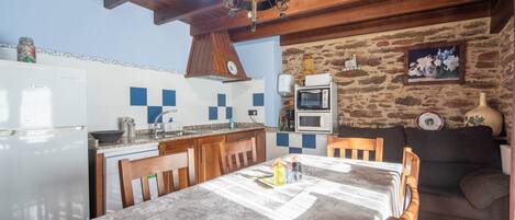 Una cocina con mesa de comedor, sillas de madera, una araña, pared de piedra y microondas.