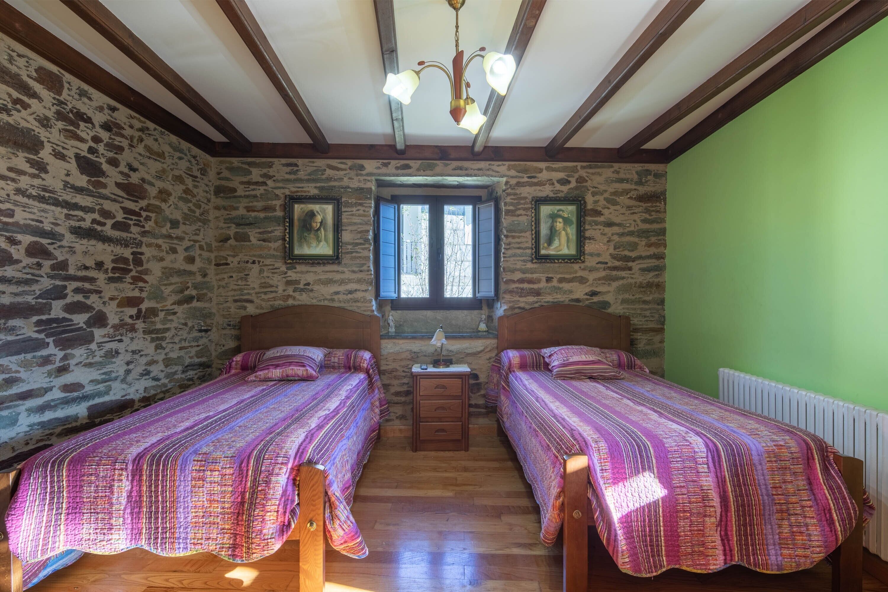 Une pièce avec deux lits en bois, un mur en pierre, une fenêtre avec des volets et un mur vert.