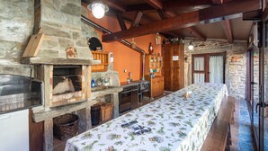 A rustic kitchen with a stone wall, wooden beams, a long dining table, and a built-in oven.