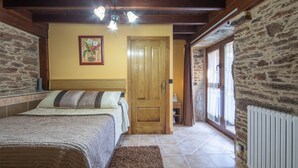 A bedroom with a wooden ceiling, a bed with a headboard, a wooden door, a radiator, and a stone wall.