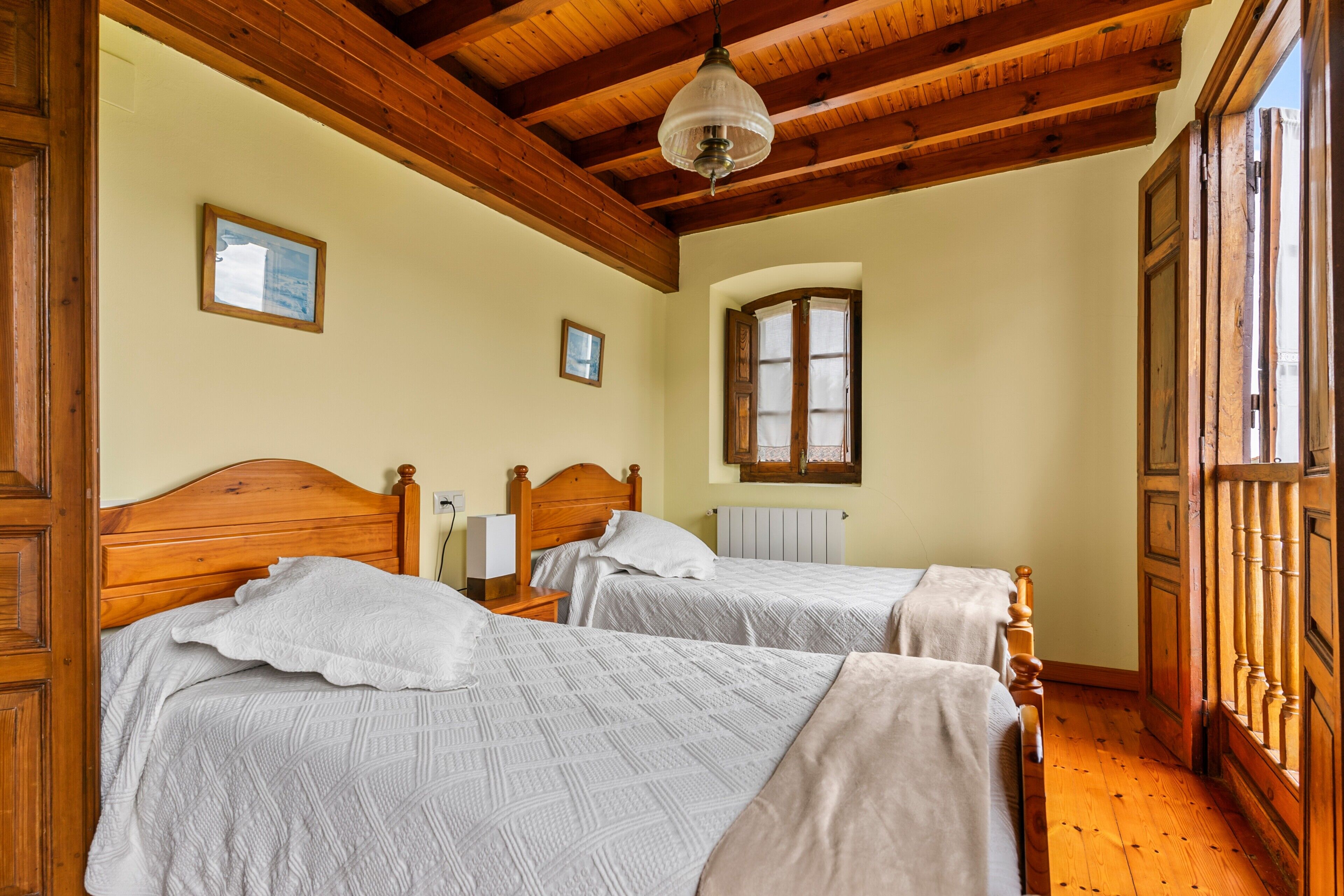 Una habitación con dos camas de madera, techo de madera, una ventana y una puerta.