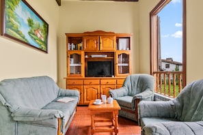 Una sala de estar con televisor, mueble de madera, dos sillones y un cuadro en la pared.