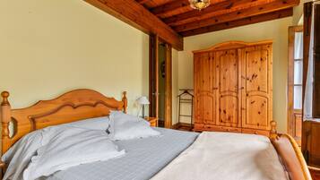 A wooden bed with a headboard, a nightstand, and a wardrobe in a room with wooden beams on the ceiling.