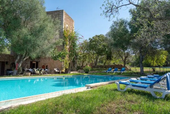 A swimming pool with lounge chairs, a stone building, and trees.