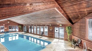 An indoor swimming pool with wooden walls and ceiling, surrounded by windows and doors.