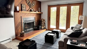 A modern living room with a fireplace, a television, and a large window with a view of trees.