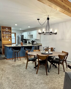 Une cuisine moderne avec des meubles blancs, un îlot central doté de tabourets et un coin repas avec une table ronde et des chaises.