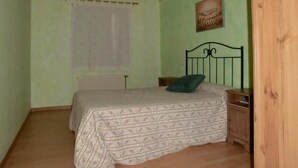 Un dormitorio con una cama, una mesita de noche, un radiador, una ventana con persianas y un ventilador de techo.
