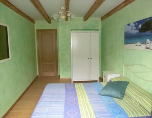 A bedroom with a bed, a wardrobe, a nightstand, and a painting of a beach scene.