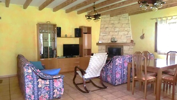 Una sala de estar con sofá, una mecedora, una mesa de comedor con sillas, chimenea y televisor.