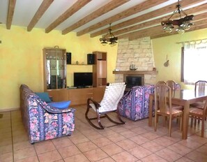 A living room with a sofa, a rocking chair, a dining table with chairs, a fireplace, and a television.