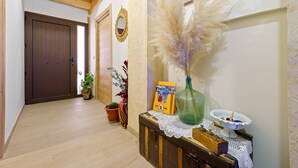 Un couloir doté d’un plancher en bois, d’une porte marron, d’un mur orné d’un miroir et d’une table sur laquelle se trouvent un vase et un tableau encadré.