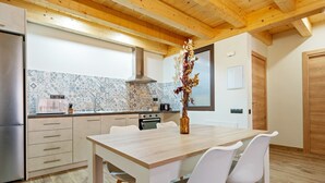 Une cuisine moderne avec un plafond en bois, un mur recouvert de carreaux, un réfrigérateur en acier inoxydable, une table à manger en bois avec des chaises blanches et un vase contenant des fleurs séchées.