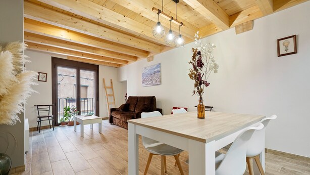 Un coin repas avec une table et des chaises en bois, un vase rempli de fleurs et une vue sur l’extérieur par une fenêtre.