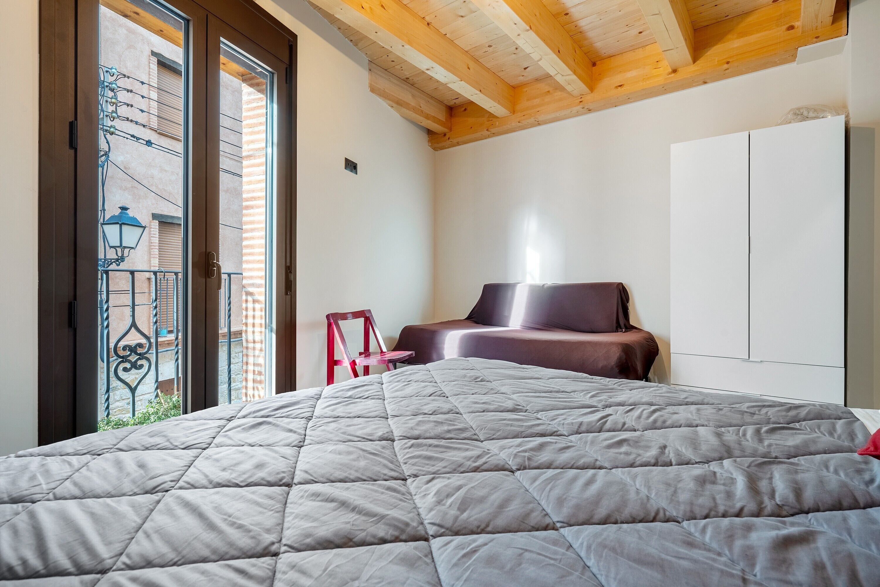 Un dormitorio con cama, una silla, un armario y un balcón con vistas.