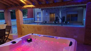 A hot tub with a stone wall and a wooden ceiling, surrounded by a patio area.