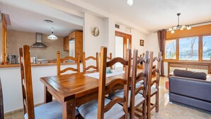 A dining area with a wooden table and chairs, a kitchen in the background, and a sofa in the living area.