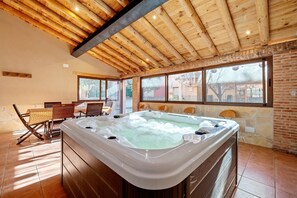 Un área de spa con un jacuzzi, vigas de madera en el techo y ventanas amplias.